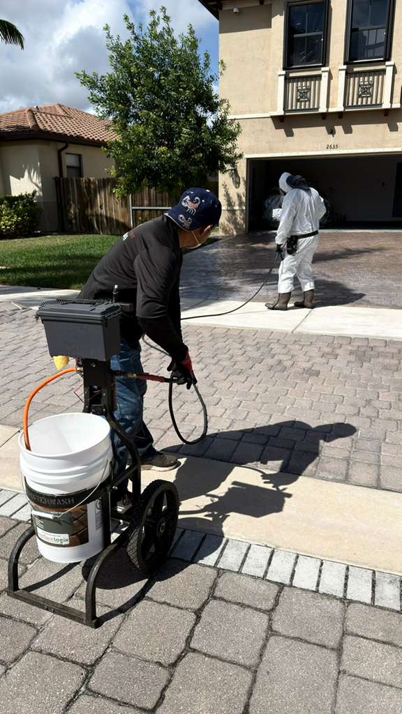 Two technicians applying sealer to a paver driveway in Miami, Florida