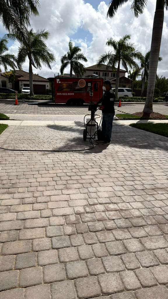 Technician spraying professional sealer onto a paver driveway in Miami